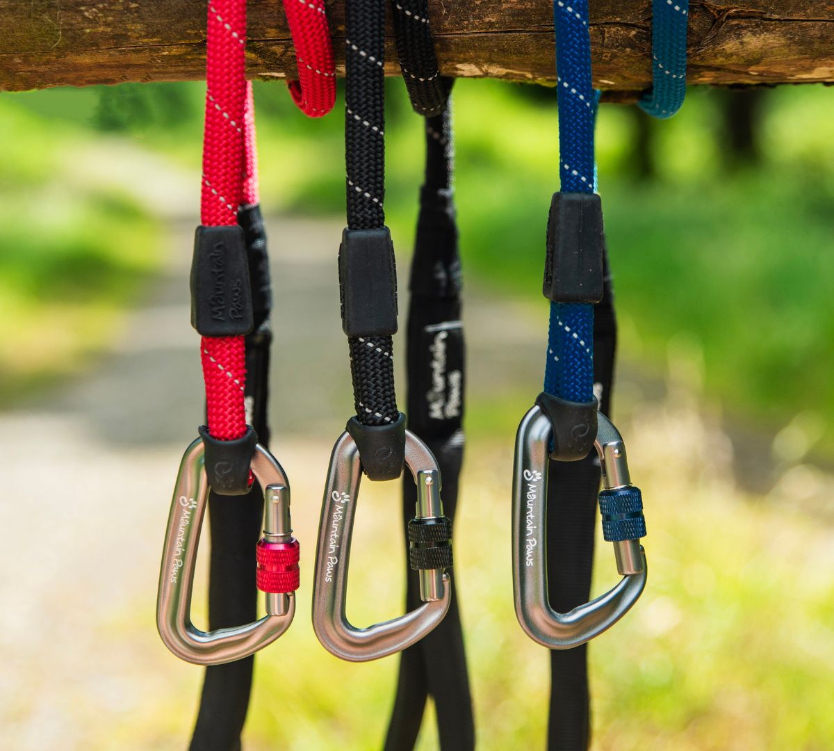 Four Mountain Paws rope dog leads hanging on a wooden beam, featuring sturdy carabiners in red, black, blue and navy.